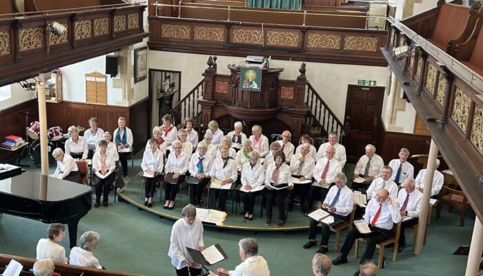 Thirty six members of the u3a Choir group performing at a summer concert event. Balconied church hall in Sherborne.