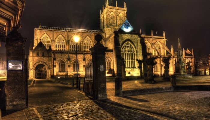 The front facade of Sherborne Abbey lit up at night.