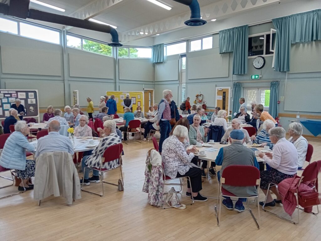 u3a Showcase event showing members sitting around tables with show boards around the room demonstrating various groups' work.