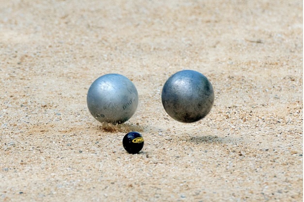 Showing a Petanque chuck with two balls one frozen in motion just about to land.