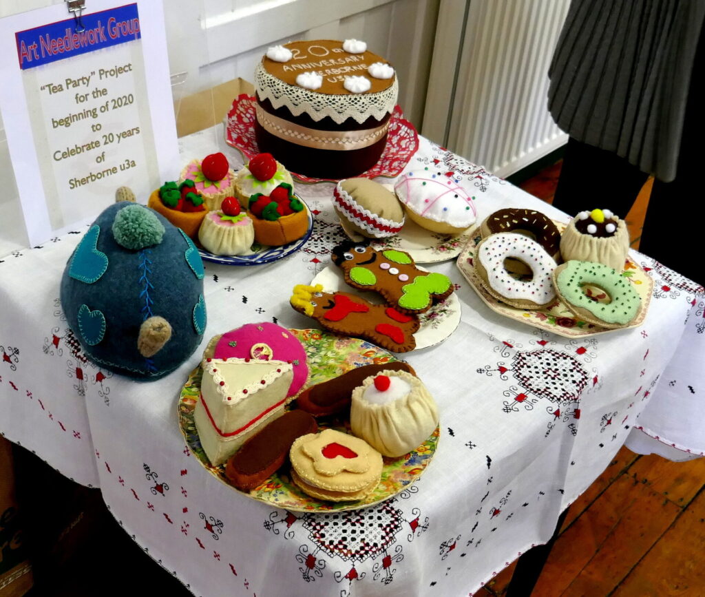 A tea table laid out with a cosy teapot and plates of cakes all sewn by members of the Art Needlework group.