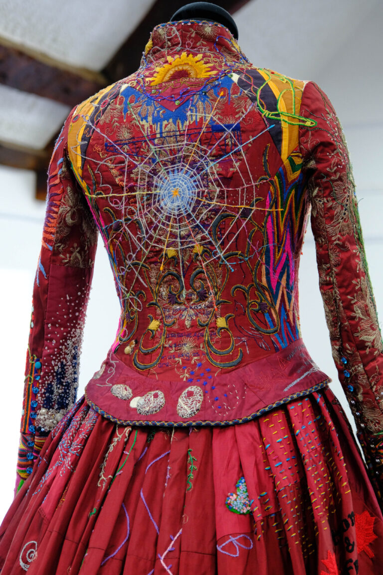Crimson dress rear vies with intricate pattern of spiders web and needlework.