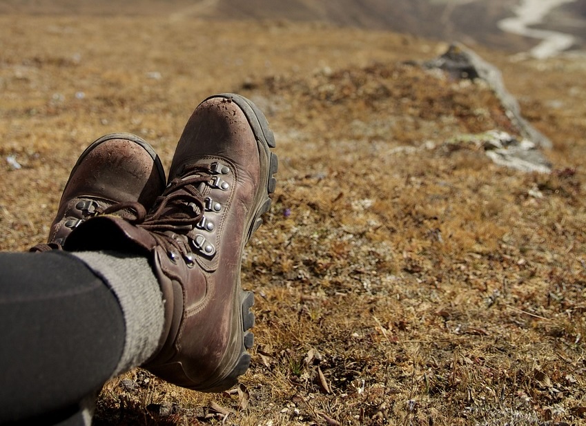 View of hiking boots with owner legs crossed and resting looking down a rocky slope.