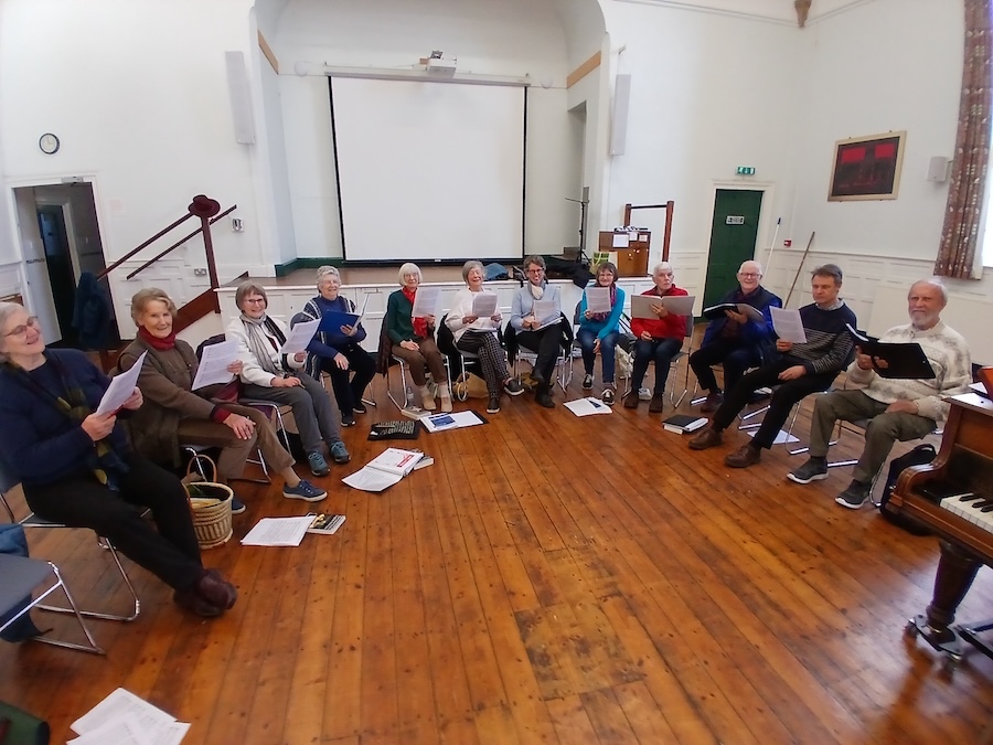 Madrigal group members seatedin a circle at a proctice session 2025.;